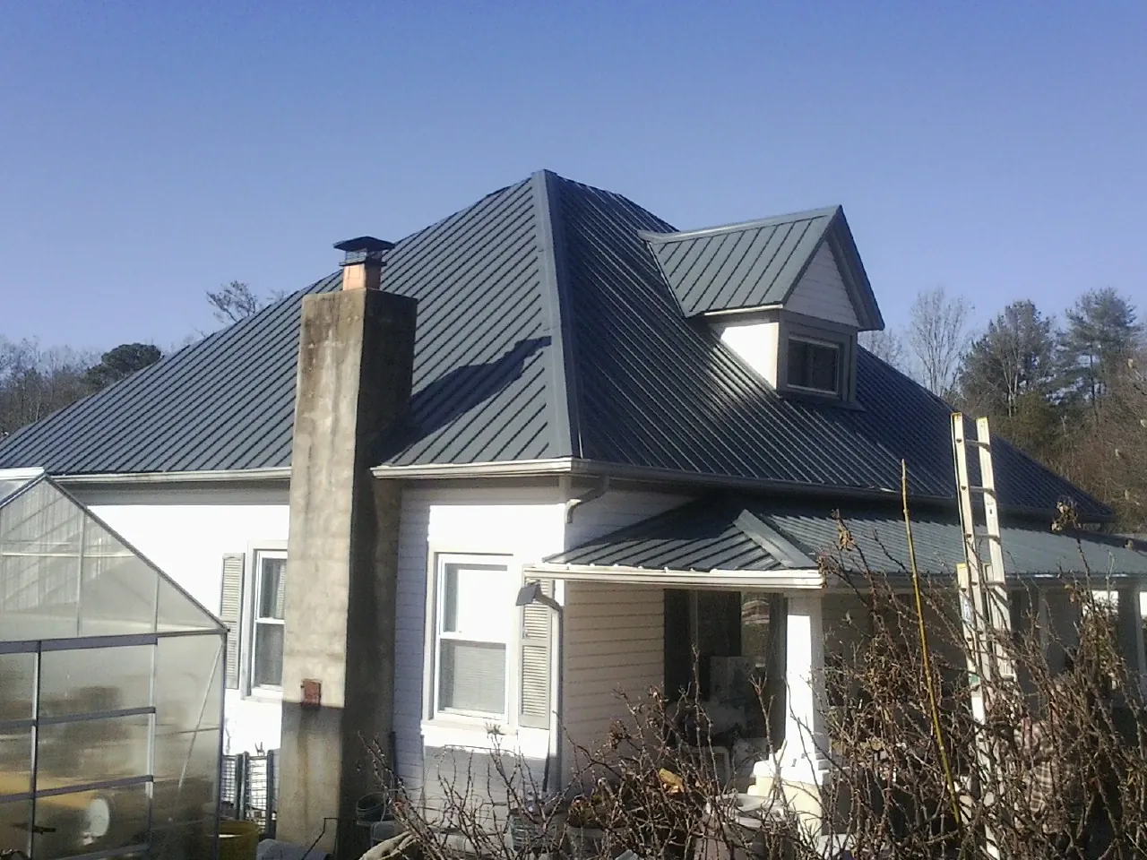 Dark blue standing seam metal roof on a white farmhouse with dormer — Slate & Tile Roof Repair by Roofing Brothers in Elkhorn