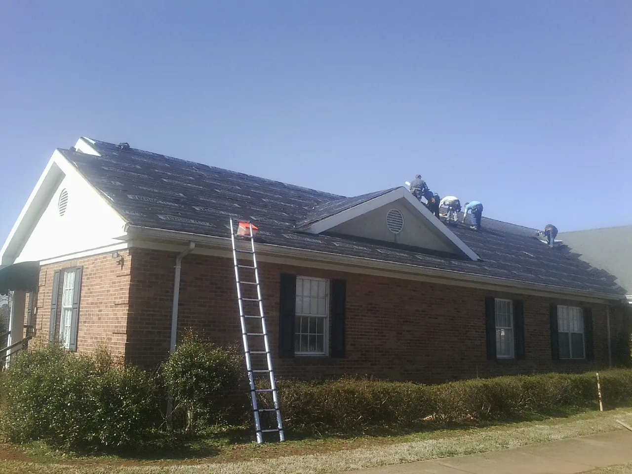 Crew tearing shingles off a brick ranch roof with a ladder set — Emergency Roof Repair work by our crew in Elkhorn