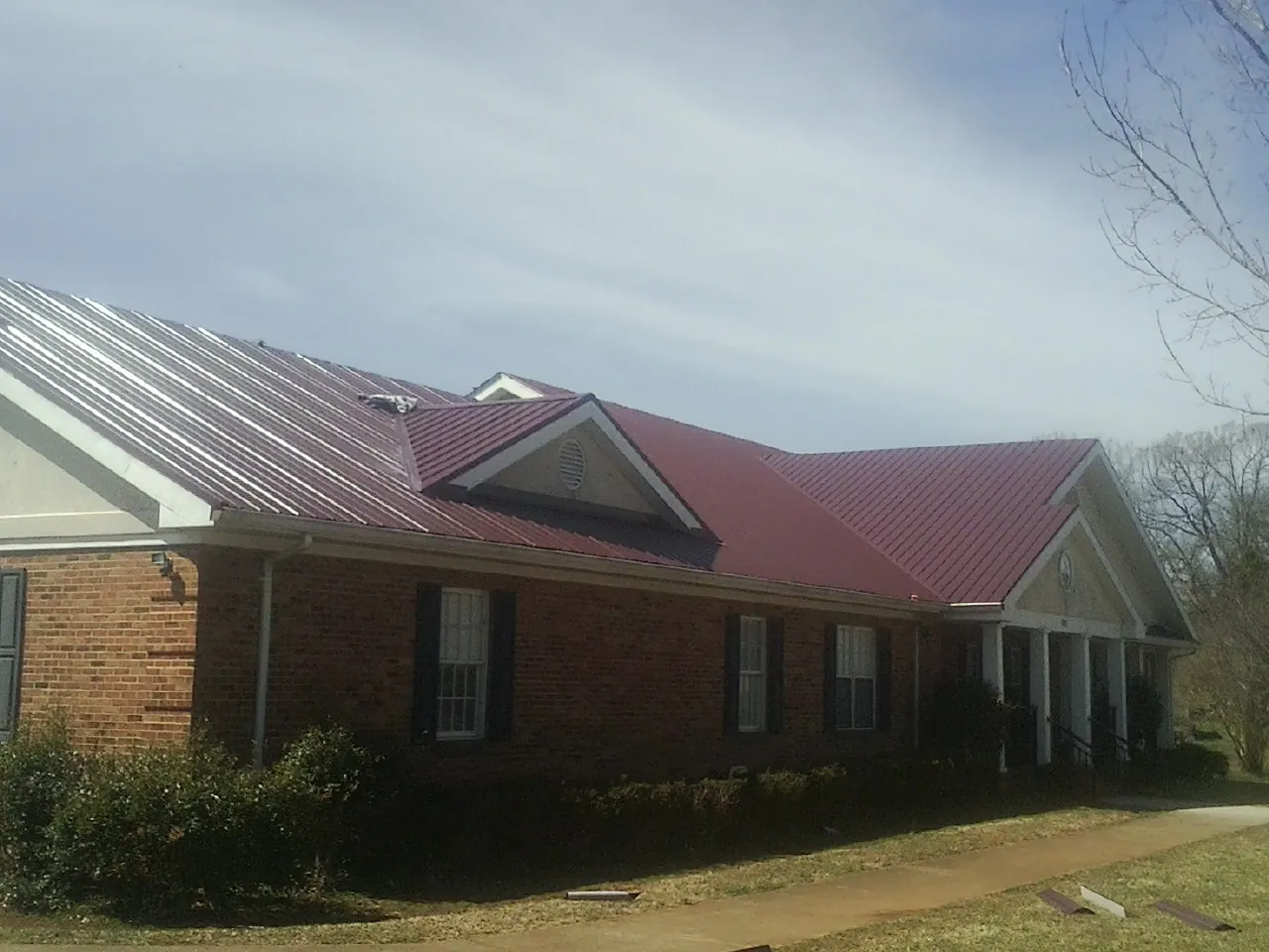 Red metal roof with gabled entries on a long brick building, from a Hail Damage Roof Repair job in Elkhorn
