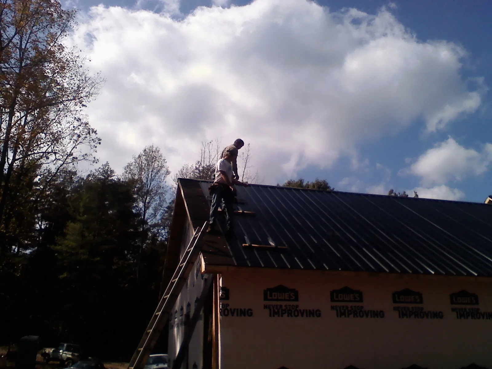 Roofer fastening dark metal panels high against a cloudy sky, from a Roof Inspection job in Elkhorn