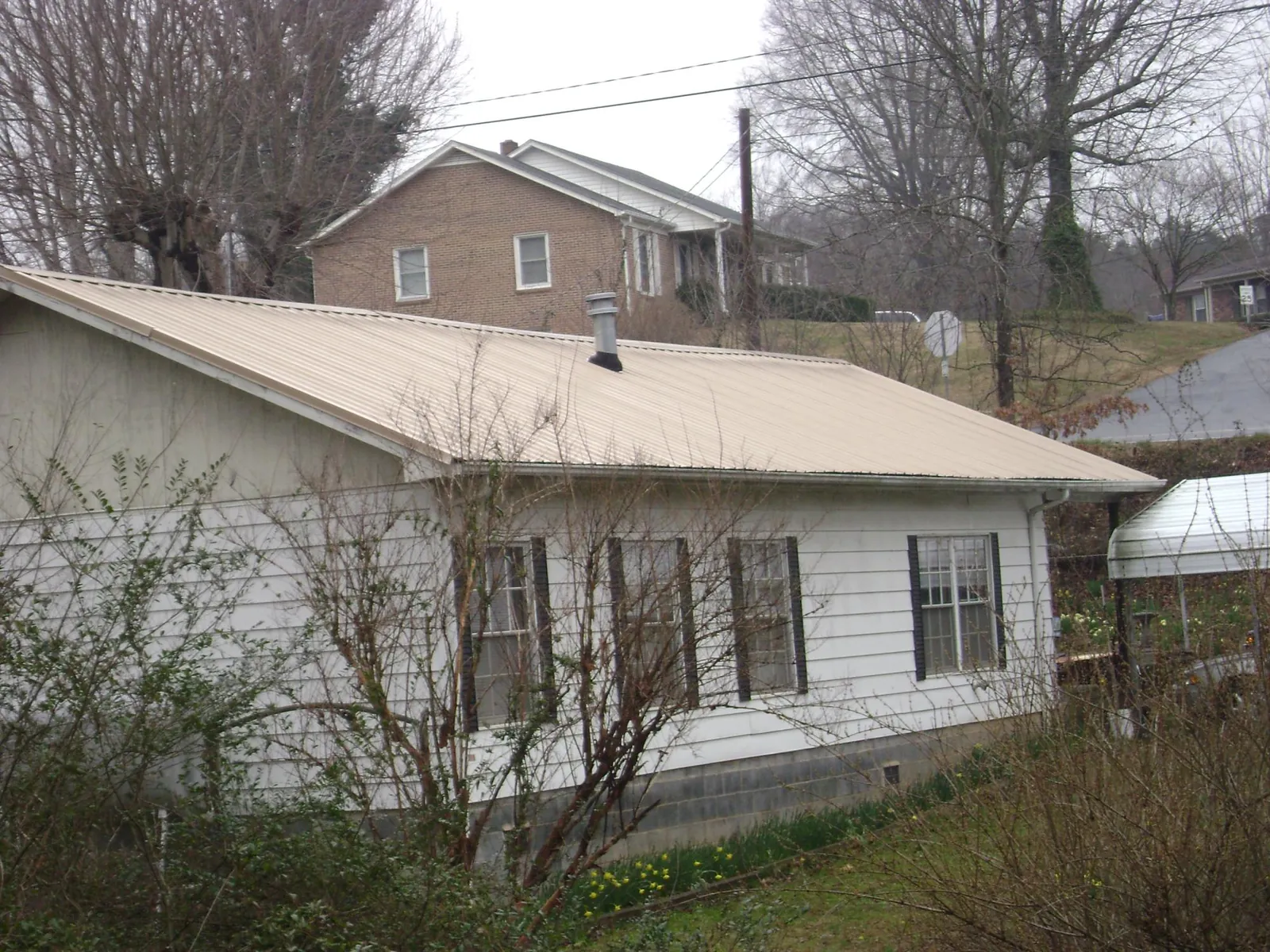 Tan metal roof on a white sided house set into a hillside — Commercial Roofing by Roofing Brothers in Elkhorn