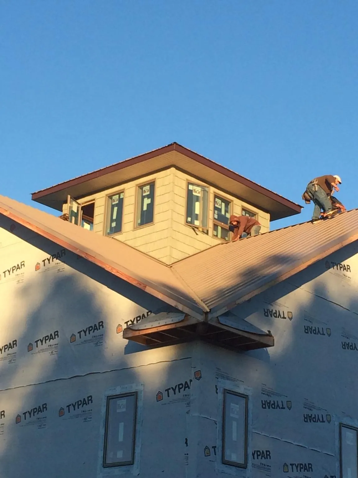 Roofers working around a rooftop cupola on a new metal roof at sunset — Roof Waterproofing in Elkhorn by Roofing Brothers